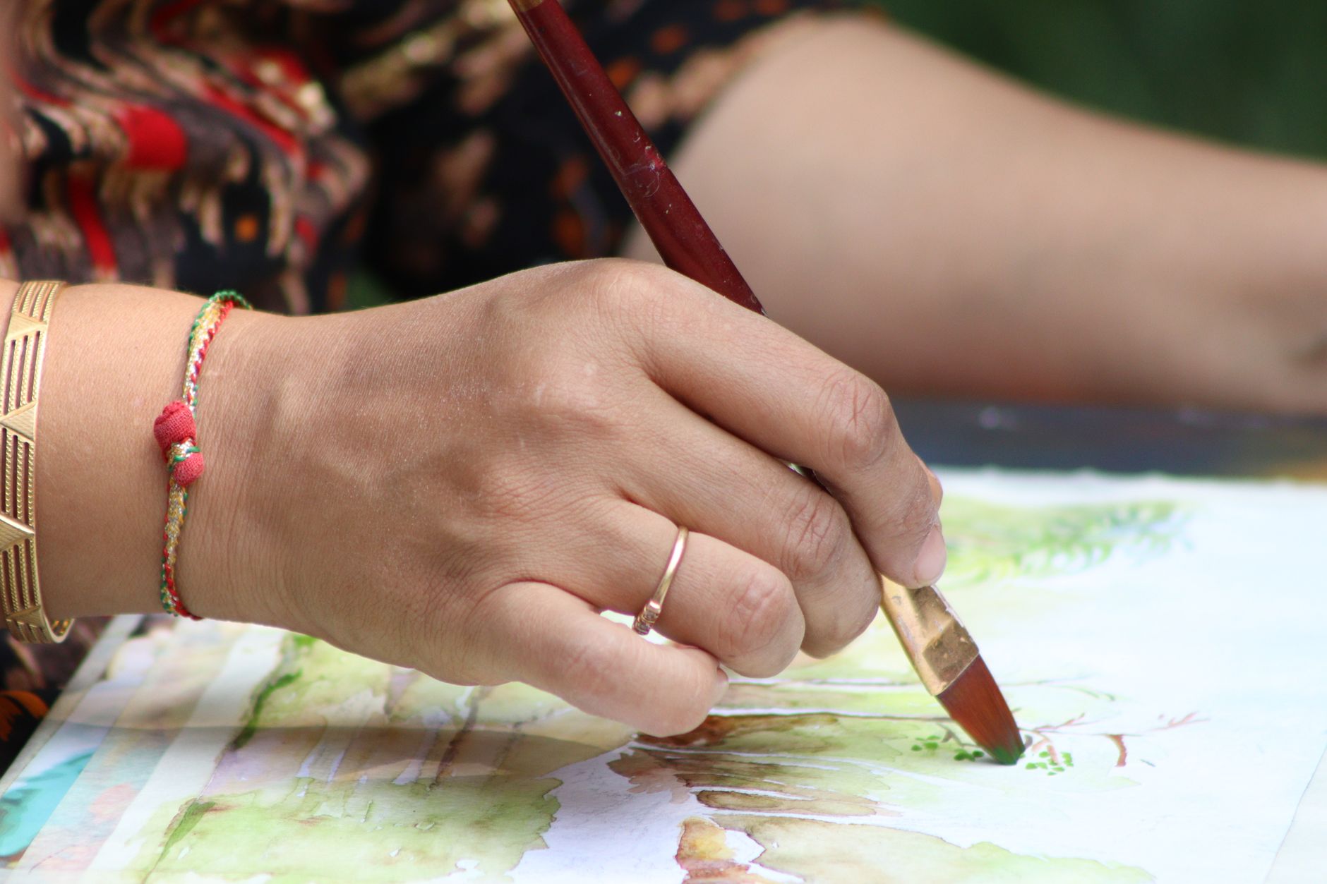 A hand painting a blue wash with a round brush on watercolour paper