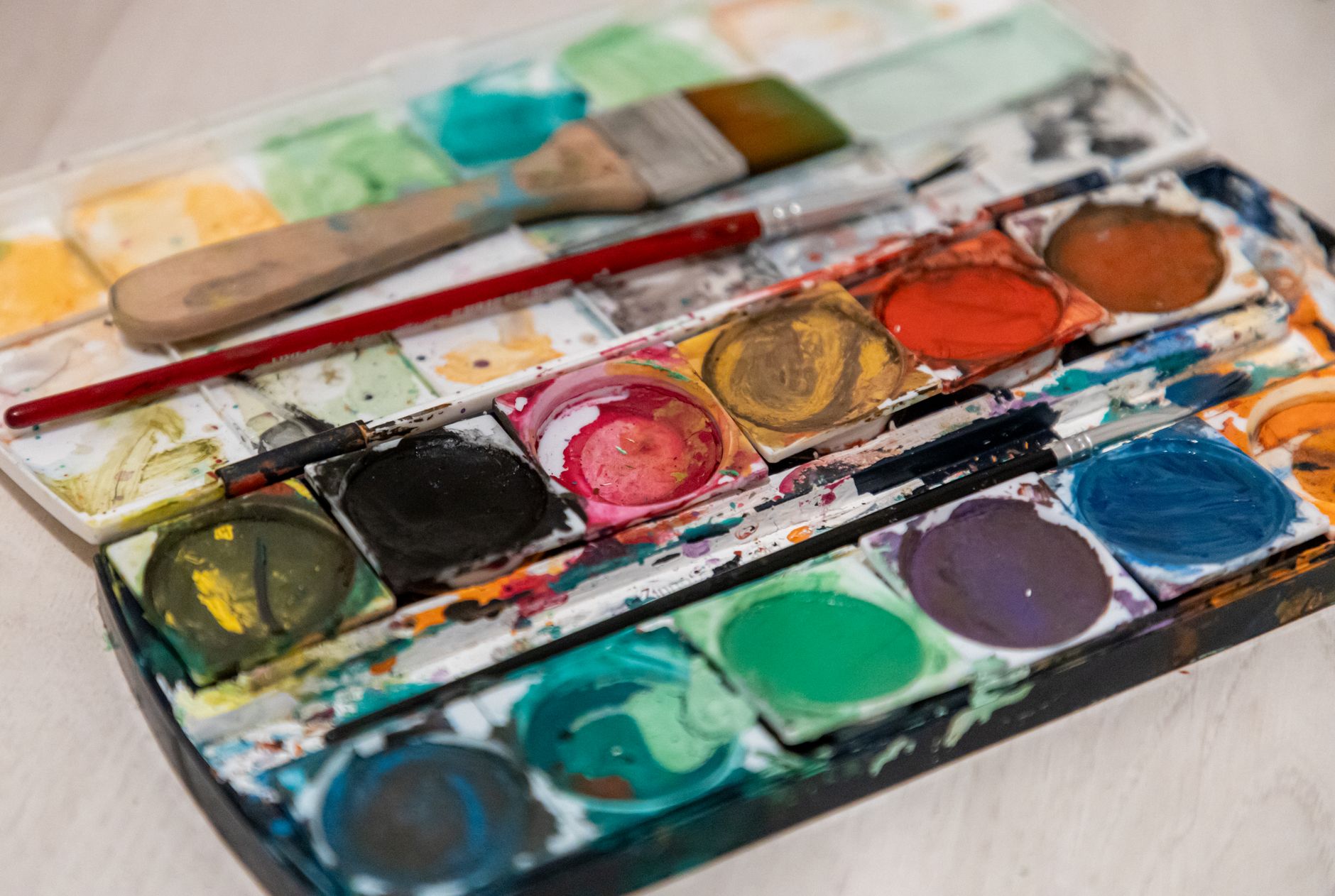 A well-used watercolour palette with brushes beside a painting